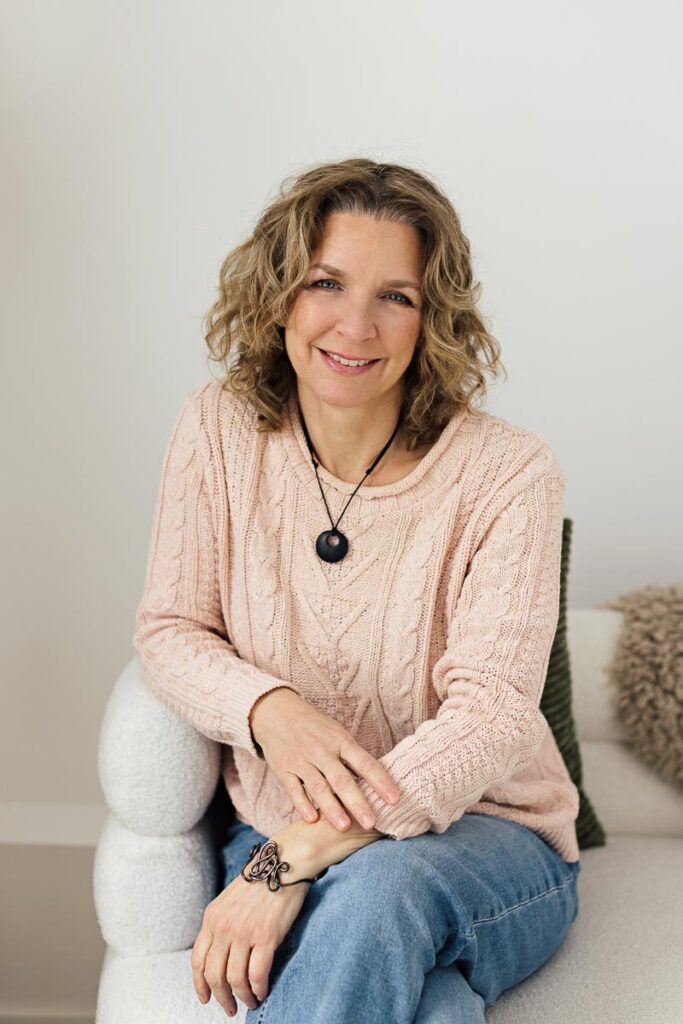 Thérapeute en relation d’aide assise dans un fauteuil, souriante, l’air accueillante, professionnelle et sécurisante.